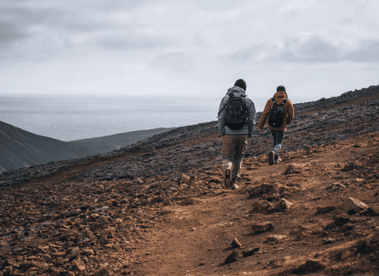 Against the backdrop of the ocean, two individuals, like partners, stroll along a mountain trail.